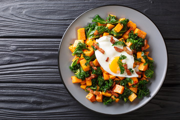 Delicious breakfast of sweet potato with kale, bacon and fried egg close-up on a plate. horizontal...