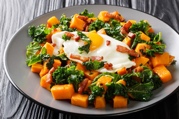 Stir fry of sweet potatoes with kale served with bacon and fried egg close-up on a plate. horizontal