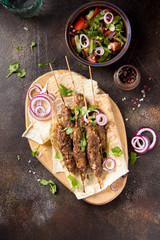 Lula kebab from minced meat (beef, lamb, veal) on pita bread (lavash), shish kebab. With red onion, cilantro and vegetable salad
