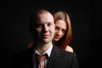 Man in black suit covers his woman with his breast.