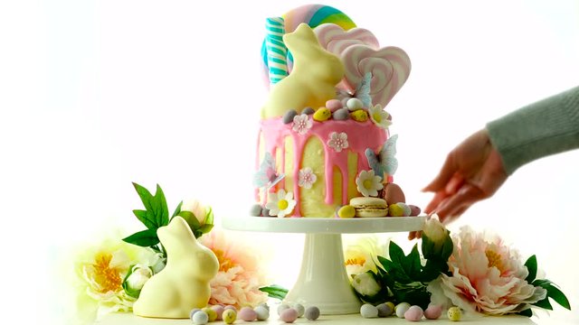 On-trend Easter theme candy land drip cake decorated with lollipops, cand eggs and white chocolate bunny on white background.