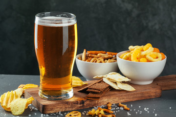 Glass of lager beer with snack bowls on dark stone background