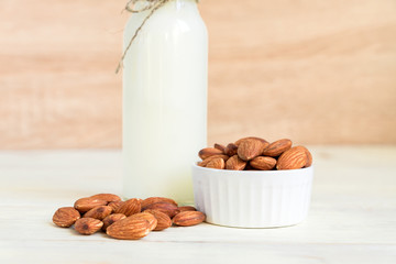 Homemade Almond milk in a bottle and nuts in white porcelain bowl on wooden background