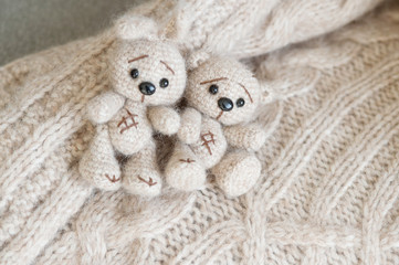 A knitted beige bunny and bear are lying on the plaid handmade of the same color.