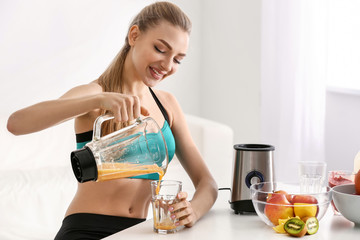 Young woman pouring healthy smoothie into glass at home