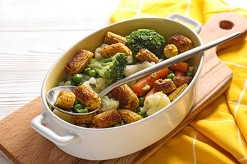 Casserole with tasty corn cobs and vegetables on white table
