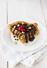 pancakes with berries and chocolate. Homemade crepe cake with chocolate cream, berries and nuts. Crepes with  chocolate on white wooden background
