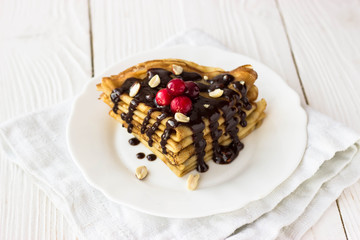 Homemade crepe cake with chocolate cream, berries and nuts. Crepes with  chocolate on white wooden background