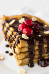 Homemade crepe cake with chocolate cream, berries and nuts. Crepes with  chocolate on white wooden background