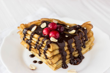 Homemade crepe cake with chocolate cream, berries and nuts. Crepes with  chocolate on white wooden background  