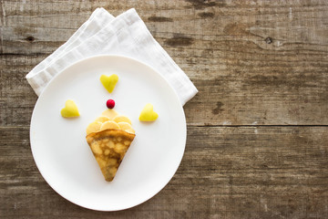 cake on a plate.  Creative idea for kid breakfast – pancakes with fruits and berries on a wooden background . Healthy and fun food for kids.