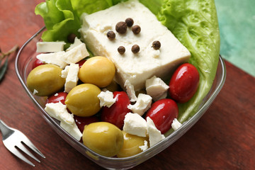 Bowl with tasty feta cheese and olives on wooden board