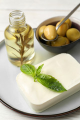 Plate with tasty feta cheese and olive oil on white table, closeup