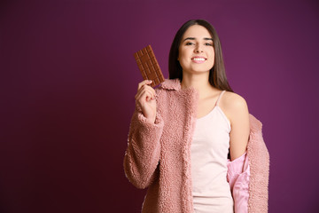 Beautiful young woman with tasty chocolate on color background