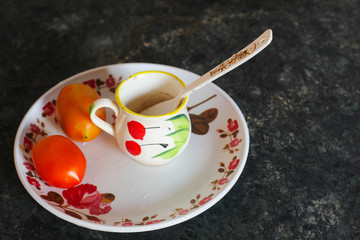 Tomato and tea cup with plastic spoon in a plastic plate on dining table