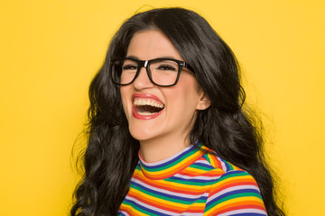 Attractive laughing brunette with glasses on yellow background