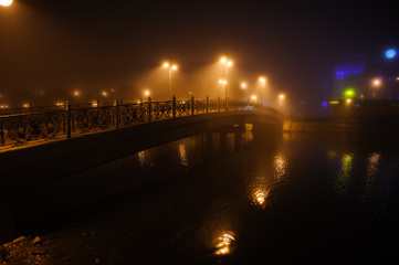 Bridge over the river in the city at night in the fog