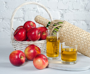 Apples and juice in glasses on  white table.