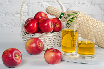 Red apples and juice in glasses on white table.