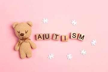 Autism concept with toy bear and word on wooden cubes on a pink background. Autism Awareness Day.
