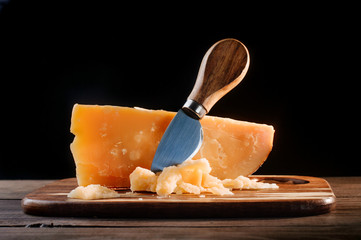 Cheese on wooden cutting board on black background with copy space