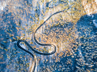 Beautiful aerial view of snow covered mountain landscape in winter time with curvy road cutting through forest. Aerial view by drone . Romania	