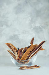 Dried banana slices in glass bowl on grey concrete background