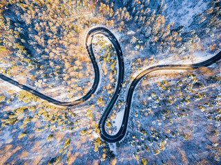 Beautiful aerial view of snow covered mountain landscape in winter time with curvy road cutting through forest. Aerial view by drone . Romania	