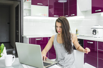 Young attractive woman working on pc at the kitchen background. Female working at computer in the morning. Freelancer at the laptop indoor. Businesswoman working home.