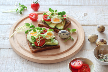 Fototapeta na wymiar Healthy sandwiches with avocado, tomato, quail eggs and sunflowers micro greens (sprouts) on a white wooden background
