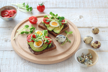 Healthy sandwiches with avocado, tomato, quail eggs and sunflowers micro greens (sprouts) on a white wooden background
