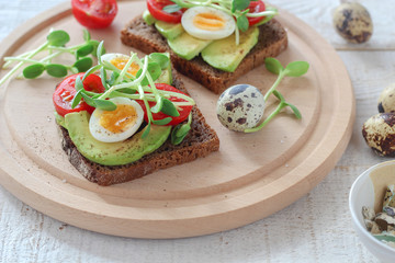 Healthy sandwiches with avocado, tomato, quail eggs and sunflowers micro greens (sprouts) on a white wooden background