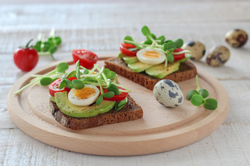 Healthy sandwiches with avocado, tomato, quail eggs and sunflowers micro greens (sprouts) on a white wooden background