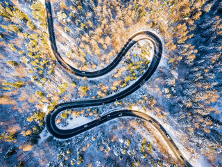 Winding road through the forest, from high mountain pass, in winter time. Aerial view by drone . Romania	