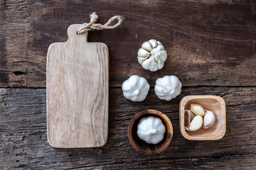 Top view of herbal vegetable ingredients, fresh garlic, and empty chopping board on old wooden table, cooking preparation concept