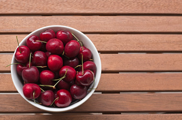 Cherries in a bowl on a wooden table, overhead view