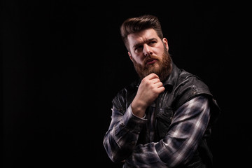 Dramatic portrait of beard man wearing a leather vest over black background