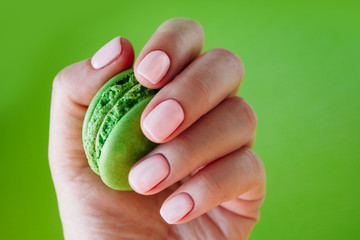 Hand with bribht green manicure with  green macaron. Isolated at bright green background.
