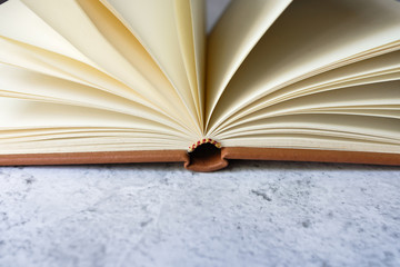 Brown leather vintage notebook blank pages open on bright white and gray concrete color texture table top with empty copy space. Education and studying concept. 