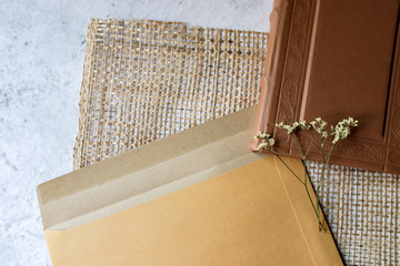 Brown leather vintage notebook, brown craft envelope, dried flower on bright white and gray concrete color texture table top with empty copy space. Education, travelling, letter, romantic concept. 