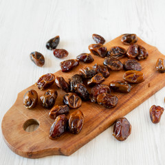 Dried dates on rustic wooden board over white wooden background, side view. Close-up.