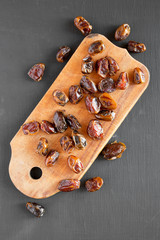 Top view, dried dates on rustic wooden board on black background. Flat lay, overhead, from above.