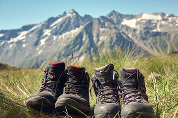 two pairs of hiking boots standing on the grass on background of mountains