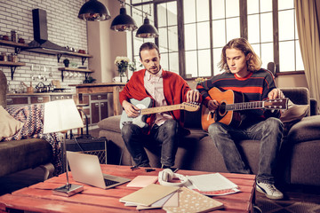Young talented musicians playing the guitar sitting on sofa at home