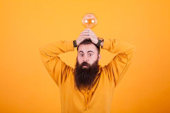 Funny bearded man with a light bulb over his head in front over yellow background
