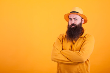 Bearded man with orange hat on his hat holding his arms crossed over yellow background