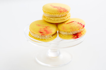 sweets, pastry and food concept - lemon yellow macarons on glass confectionery stand over white background
