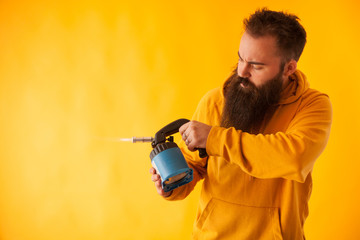 Bearded handy man holding blow torch over yellow background