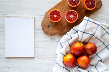 Whole and halved blood oranges, blank notepad, overhead view. Flat lay, top view, from above.