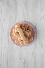 Savoyardi biscuits or ladyfingers cookies on pink plate over white wooden surface, top view. Flat lay, overhead, from above.